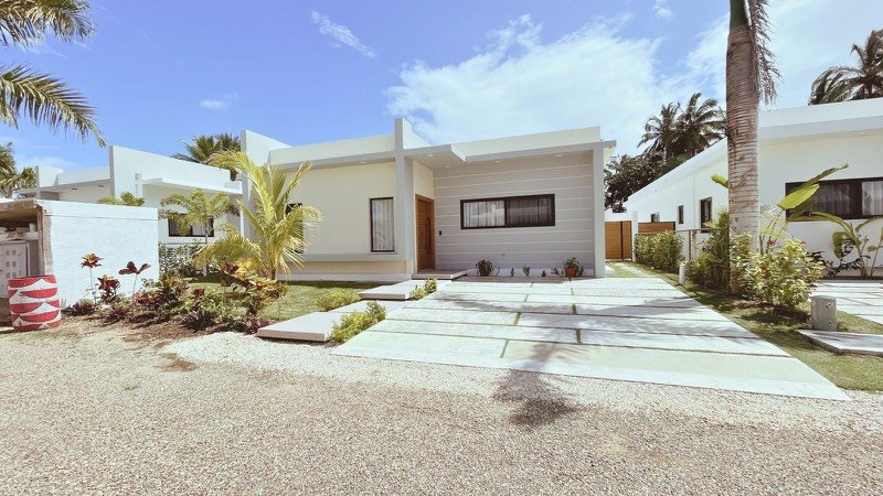 Fotografía exterior de una villa moderna blanca con una entrada bordeada de palmas