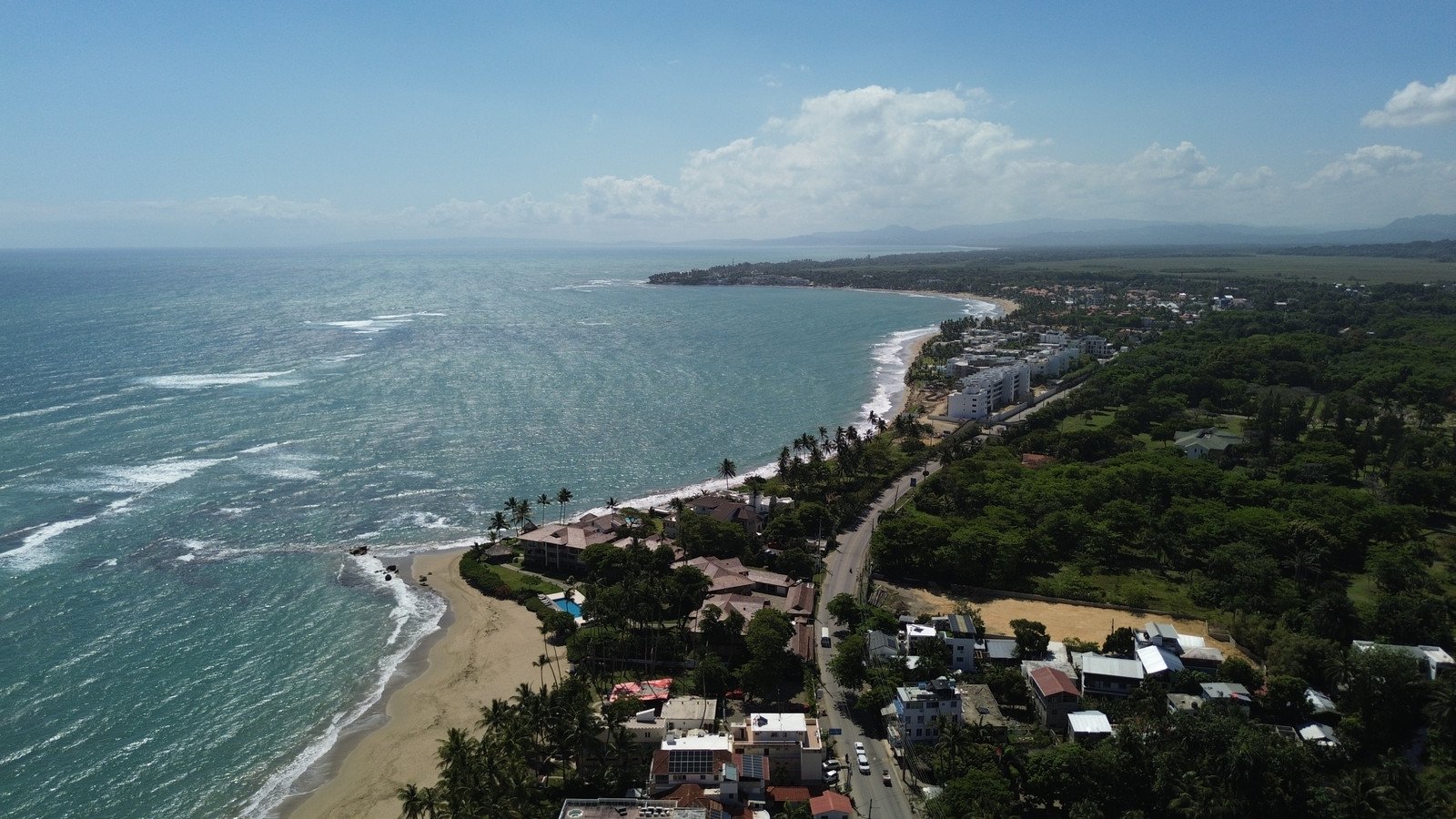 Vista aérea de una bahía de la Costa Norte con olas rompiendo y casas frente al mar, República Dominicana